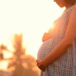 A pregnant woman holding her belly at sunset