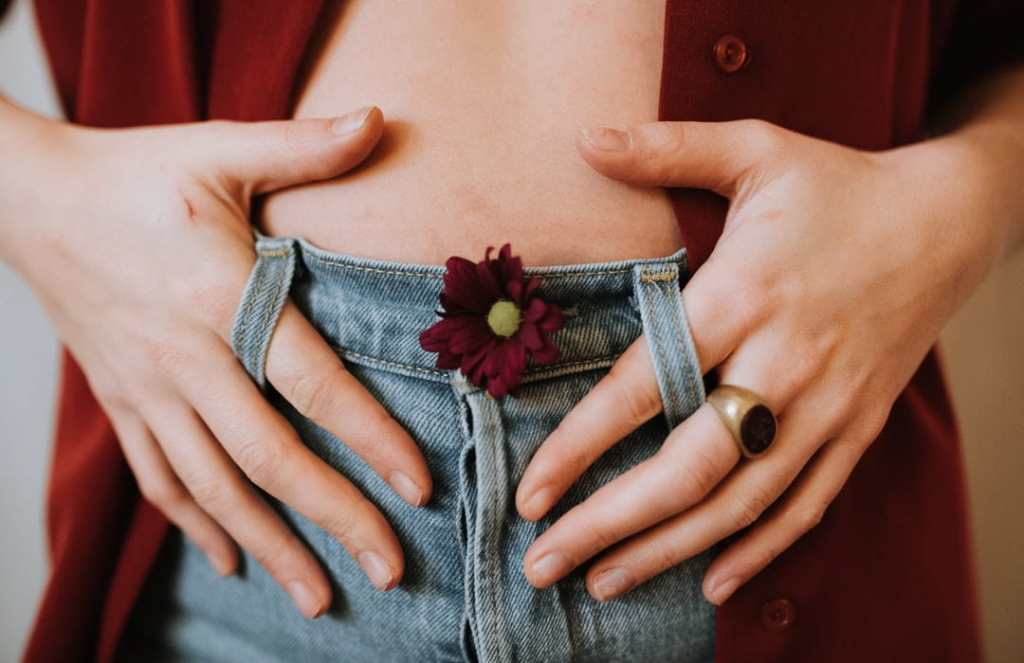 Woman holds belly with red flower in her blue jeans