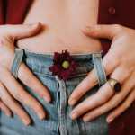 Woman holds belly with red flower in her blue jeans