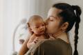 Mother with black hair in a braid holding and kissing baby