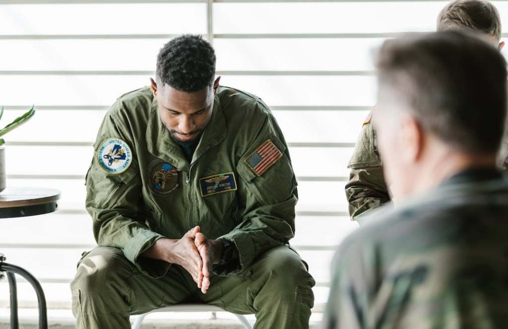 Soldier sitting with hands together in a group of other soldiers in the backround