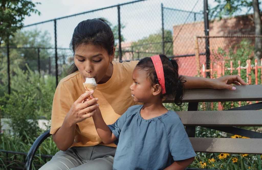 Daughter feeds her mom ice cream in park in summertime