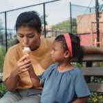 Daughter feeds her mom ice cream in park in summertime