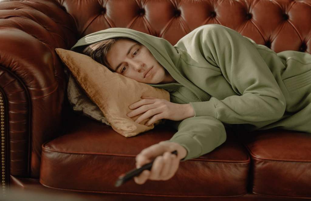 woman-in-gray-hoodie-lying-on-brown-leather-couch