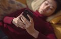 Woman lying down holding black smartphone.
