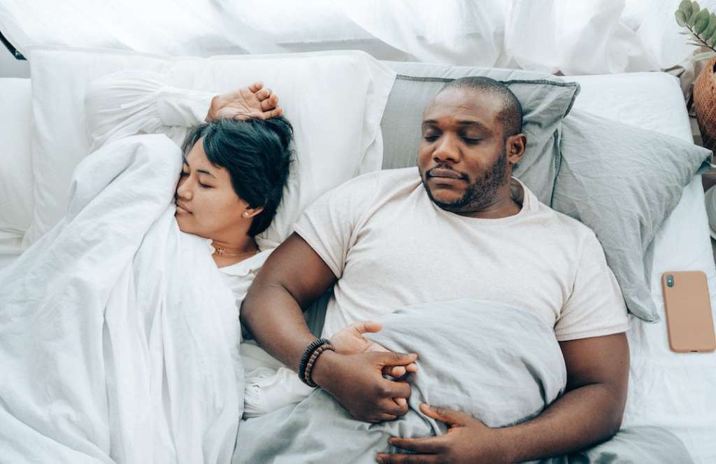young-multiethnic-spouses-sleeping-in-bed-holding-hands