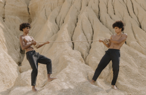 Two teen boys play tug of war barefoot on a rock