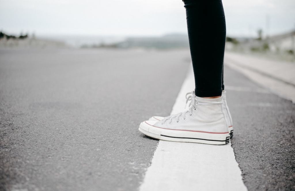 Someone stands on a white road line in white converse high tops