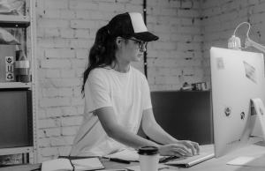 Young woman in white t-shirt and baseball caps works on a desktop computer