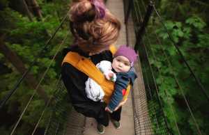 Mom walks baby in baby carrier across suspension bridge in a forest