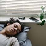 youngster-sleeping-near-gadgets-in-bedroom