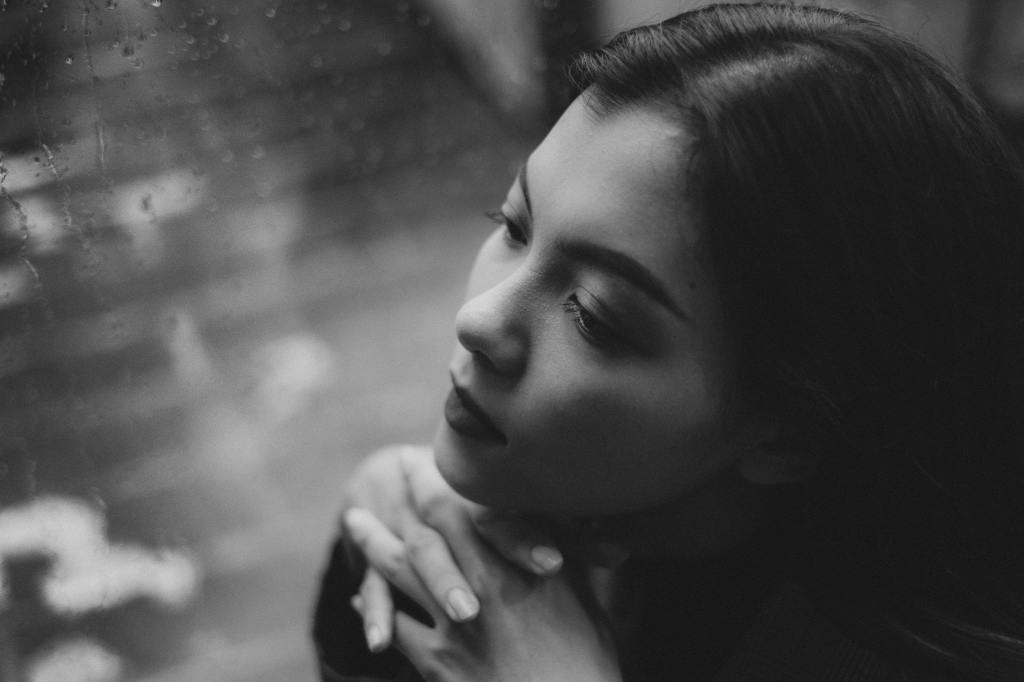 teen girl sitting near wet window while it's raining