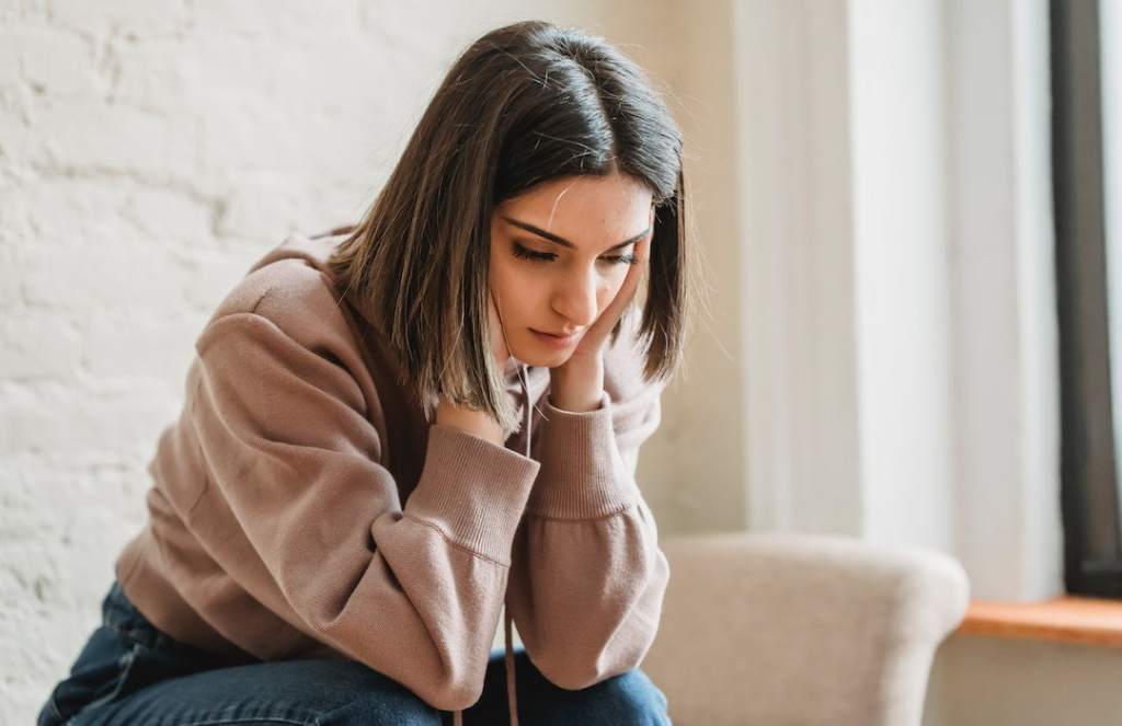 Sad woman sitting on couch in pink sweater