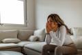 Woman in a white shirt and brown leggings sitting on a couch looking worried