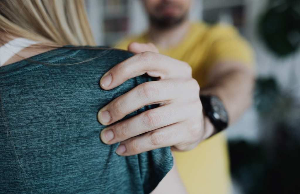 white man wearing yellow with black watch grabs woman's shoulder