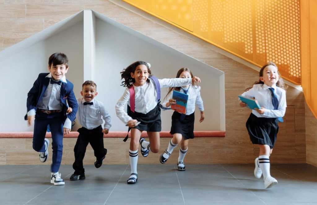 Five children in school uniforms running indoors