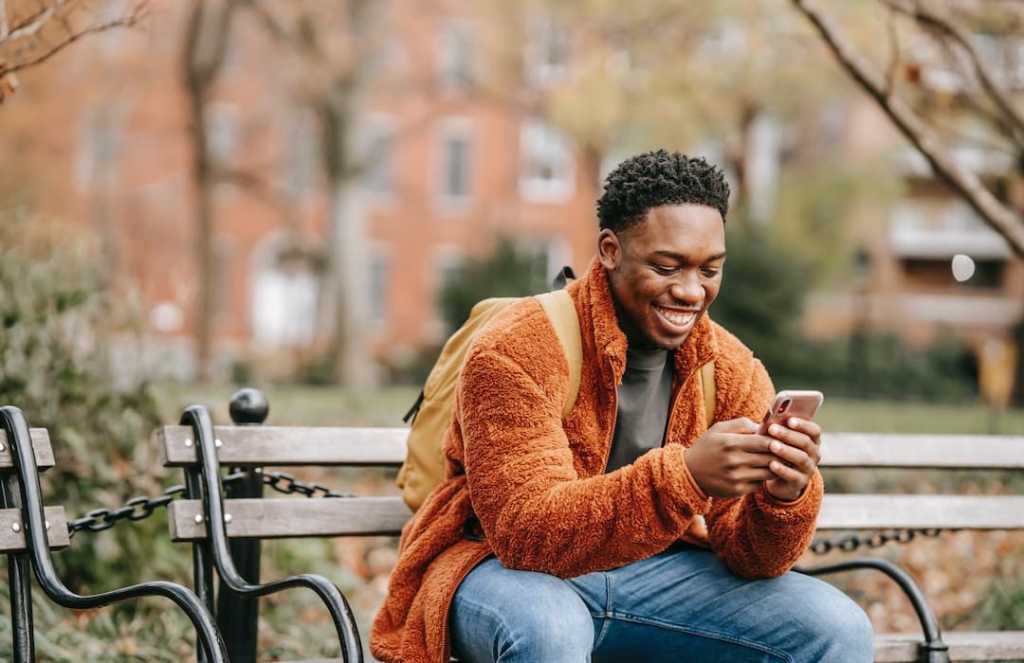 Delightful African American man surfing modern cellphone in city park