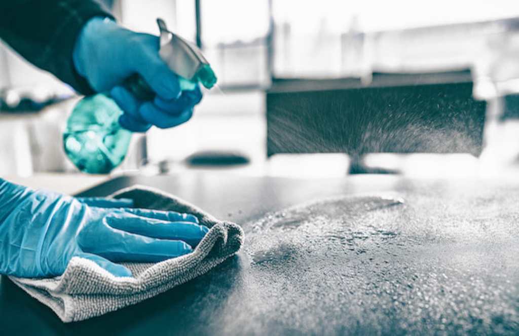 Person cleaning counter with disinfectant spray and microfiber towel