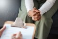 Woman's hands clasped waiting in front of a prescriber with a clipboard