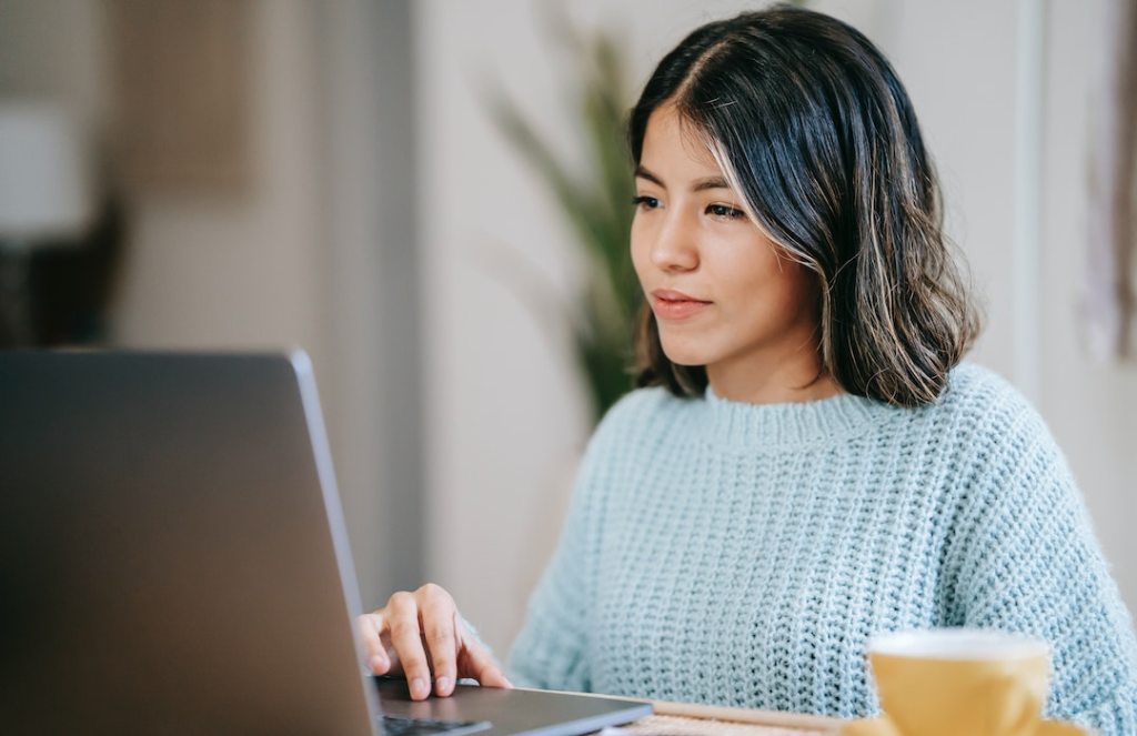 Hispanic female student using laptop near tea mug in room