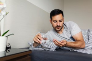 Man laying in bed about to take antidepressant with glass of water