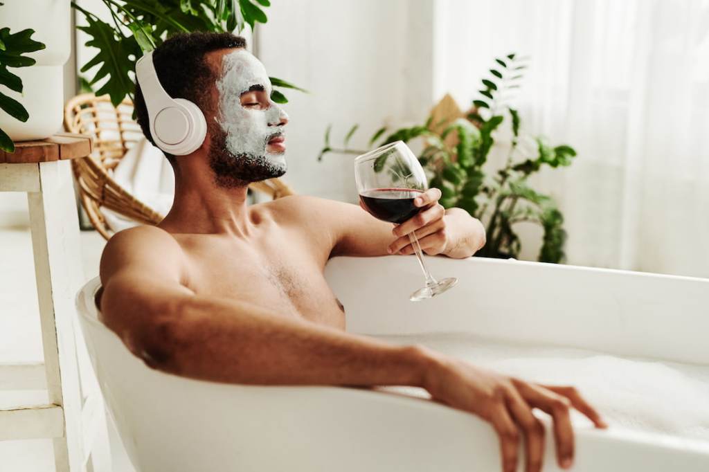 Man listening to music and drinking wine in the bathtub