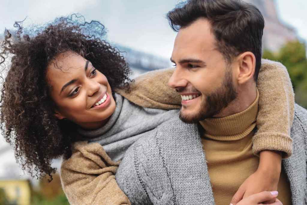 Couple wearing fall attire smiling romantically at each other