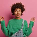 Woman in a green sweater trying to relax in front of pink background