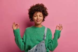 Woman in a green sweater trying to relax in front of pink background