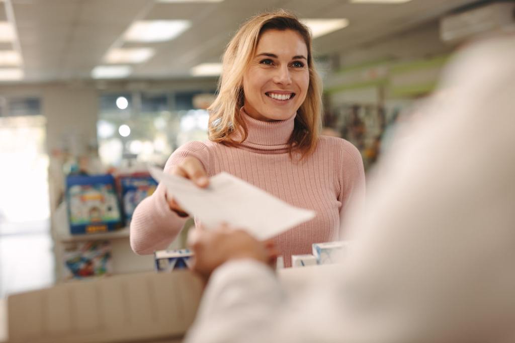 Happy woman handing prescription to chemist at pharmacy