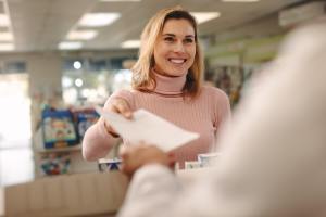 Happy woman handing prescription to chemist at pharmacy
