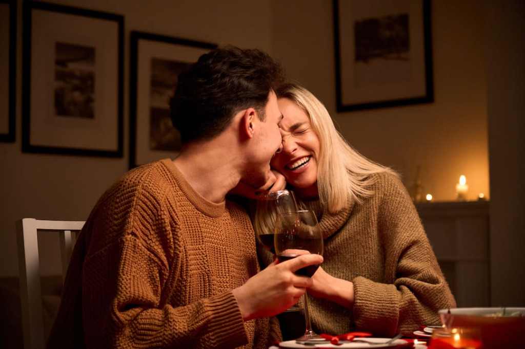 Romantic couple wearing sweaters together while drinking red wine at the table