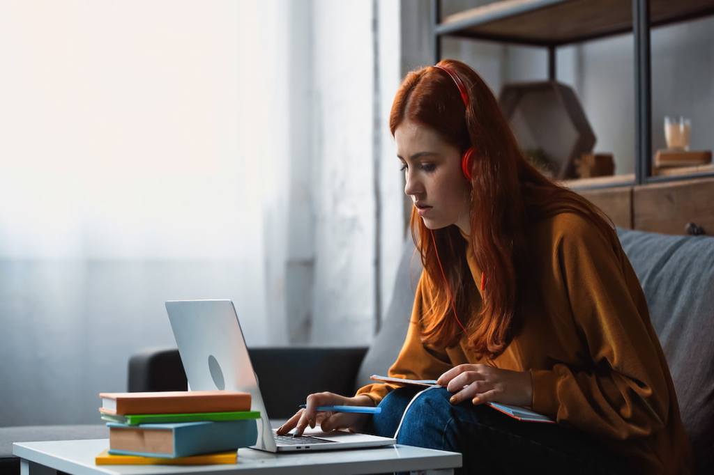 White student wearing orange studying at table with window in the background