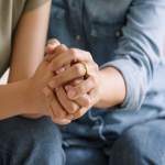 Two people wearing jeans holding hands together while sitting on a couch