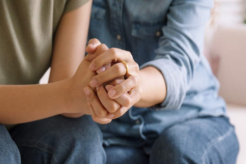 Two people wearing jeans holding hands together while sitting on a couch