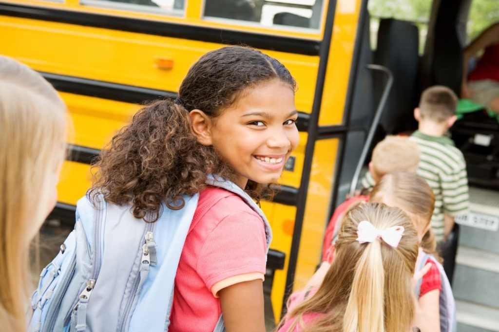 Child with a blue backpack boarding a school bus with other students