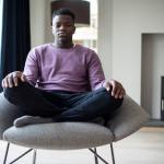Black teenager in a purple shirt meditating in the living room