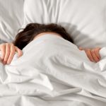 Woman with white bedsheets pulled over her eyes