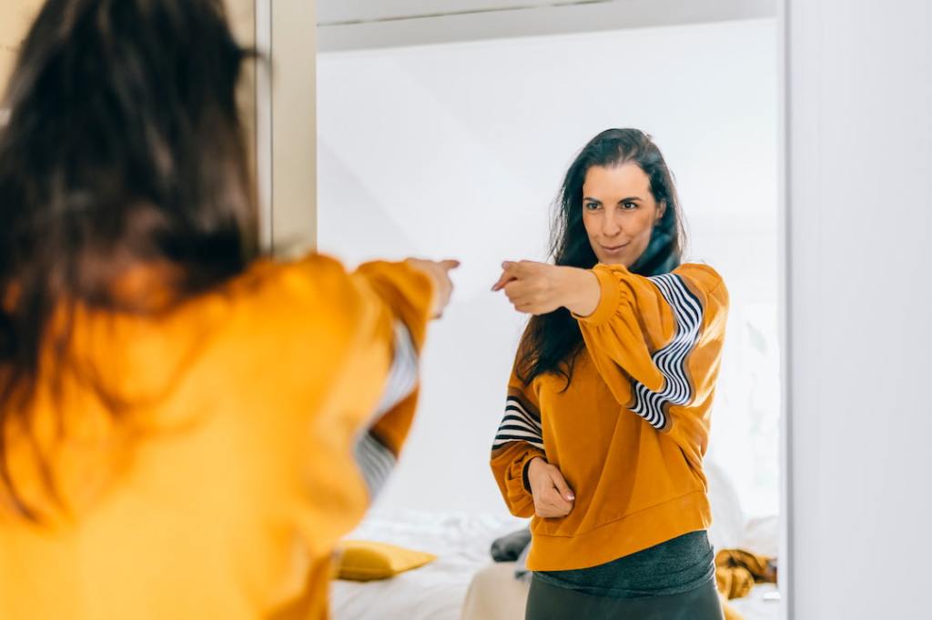 Woman in a yellow shirt giving herself a pep talk in the mirror