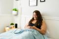 Woman sitting up in bed and smiling while looking at her phone