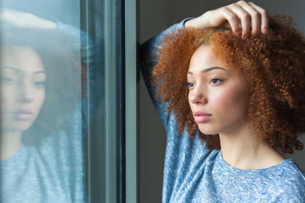 Red-haired woman looking out the window with a light blue shirt on