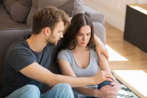 Man with his arm around a woman as they both sit on the ground in a living room