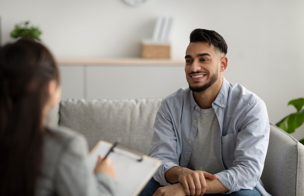 Happy middle eastern man talking to his psychologist, sharing therapy results with counselor, receiving professional help at mental health clinic