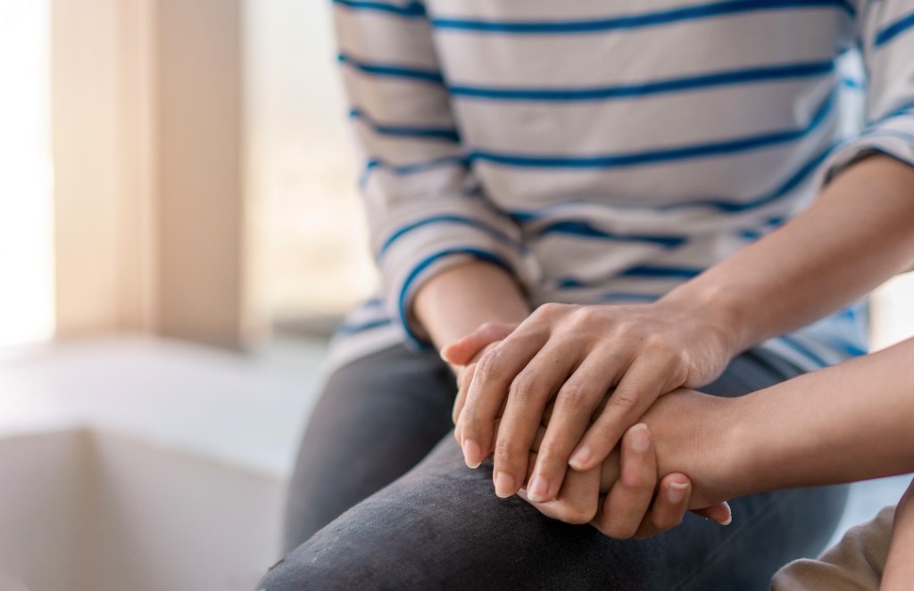 Young woman sitting and touch young depressed asian woman for encouragement near window