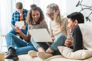 Three teenagers sitting on a couch looking at a laptop