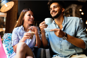 A young woman and man smile at one another while drinking coffee in arm chairs