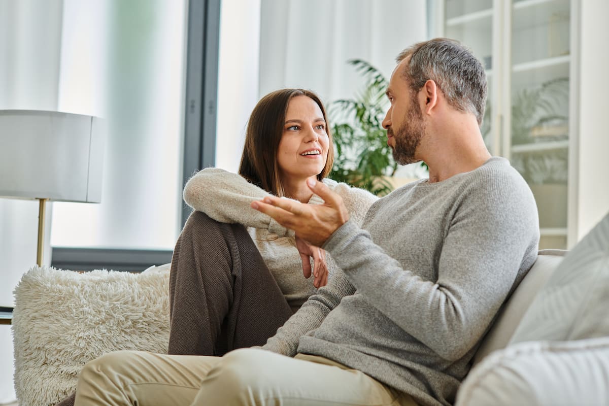 Man and woman talking on a gray couch in a living room