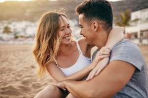 Woman and man with arms around each other sitting on the beach at sunset