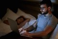 Businessman lying on bed and working with laptop late at night..
