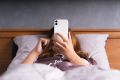 Woman under pink blankets on her phone in bed during the day
